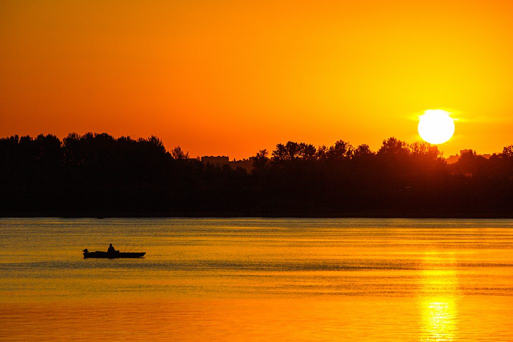 Fisherman in a boat floating on the river at sunset